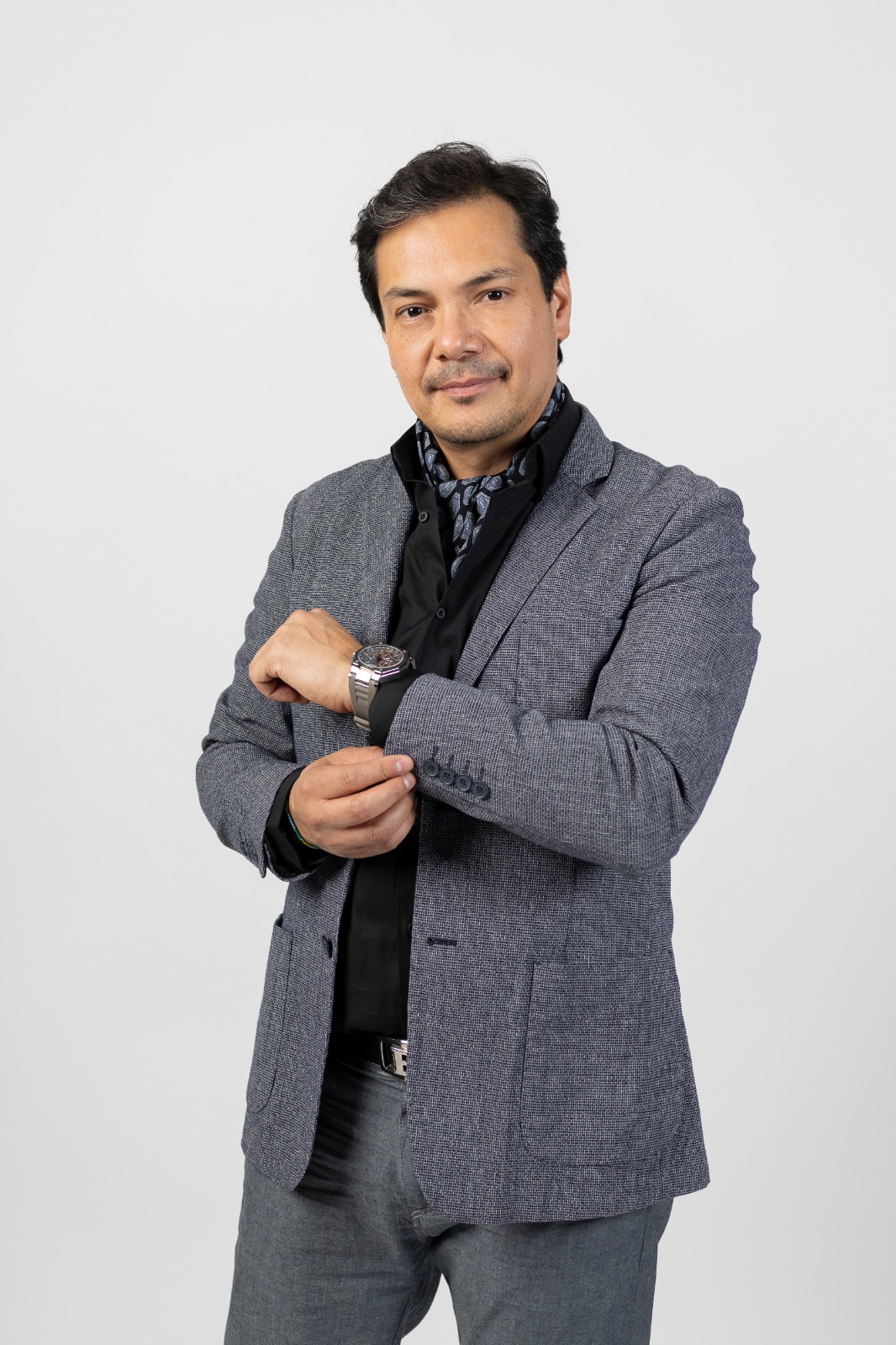 Dr. David Alcántar — traje gris, viendo el reloj