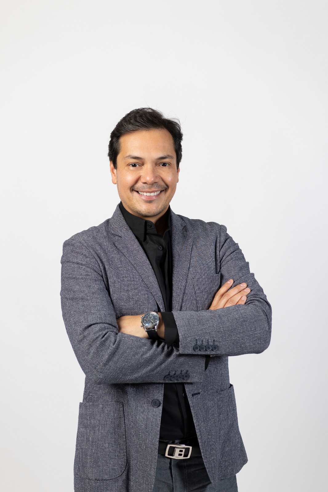 Dr. David Alcántar — traje gris, brazos cruzados